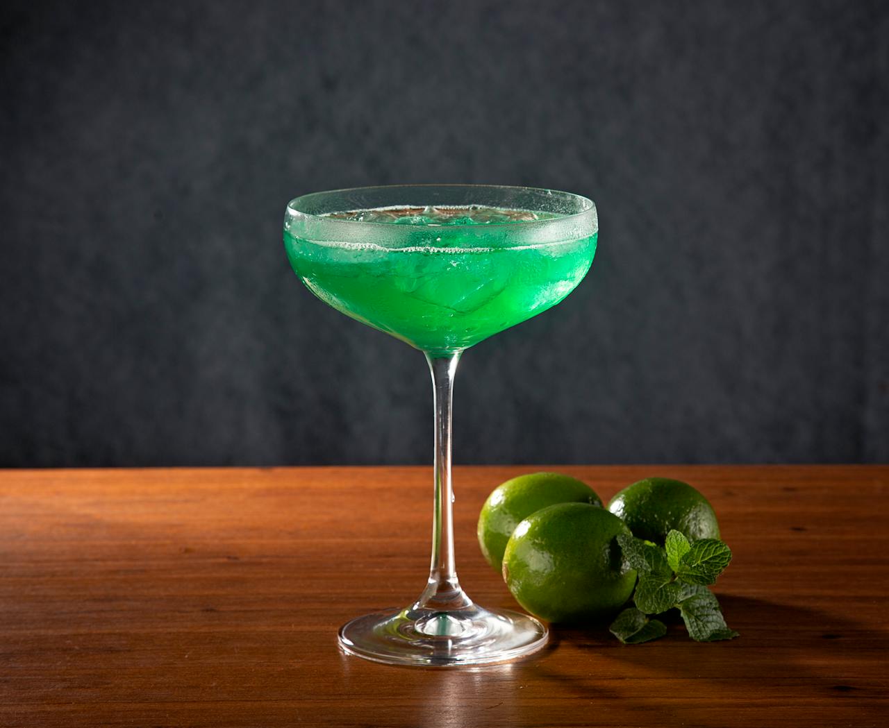Home A refreshing green cocktail served in a coupe glass, garnished with fresh limes.