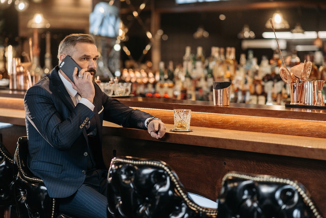 Home Elegant businessman in a suit making a phone call at a luxury bar with a glass of whiskey.