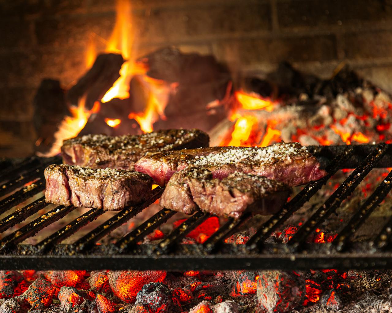 About Succulent steaks grilling over hot coals and flames for a mouthwatering cookout.